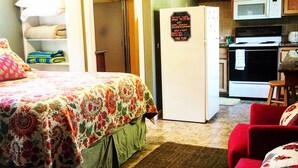 Un dormitorio con una cama, refrigerador, microondas y una pequeña kitchenette.