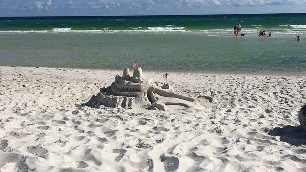 Ein sandiger Strand mit Fußabdrücken und einer Sandburg mit Wimpeln.