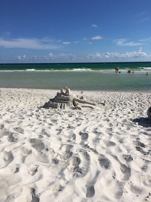 Una playa arenosa con huellas y un castillo de arena con banderas.