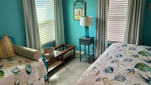 Ein Zimmer mit türkisfarbenen Wänden, zwei Betten mit blumigen Überdecken, einem kleinen Tisch mit einer Lampe und einem gerahmten Bild an der Wand.