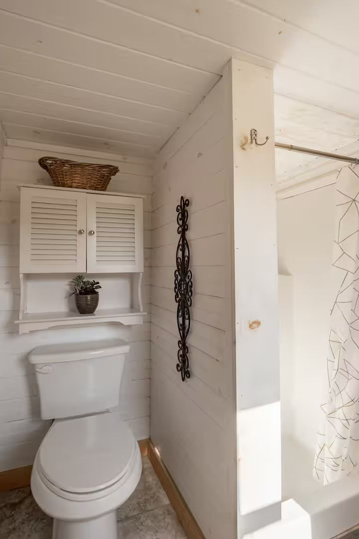 Un bagno con il water, un mobile bianco con un cesto sopra e un elemento decorativo in metallo sulla parete.