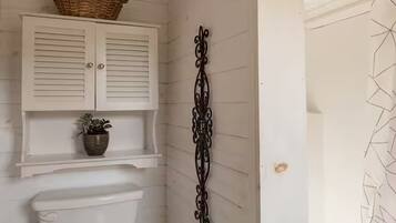 Un bagno con il water, un mobile bianco con un cesto sopra e un elemento decorativo in metallo sulla parete.