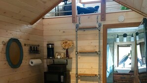 A cozy room with a loft bed, a small kitchenette, a mirror, and a door leading to another room. - Red Tiny House In The Mountains - waterfall, jacuzzi and stunning farm views (Clayton)