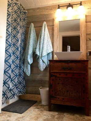 Ein Badezimmer mit Holzwand, Waschbecken mit Spiegel und Duschvorhang mit geometrischem Muster.