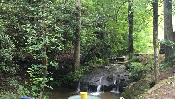 A deck with two chairs and a table, overlooking a waterfall in a forested area. - Red Tiny House In The Mountains - waterfall, jacuzzi and stunning farm views (Clayton)