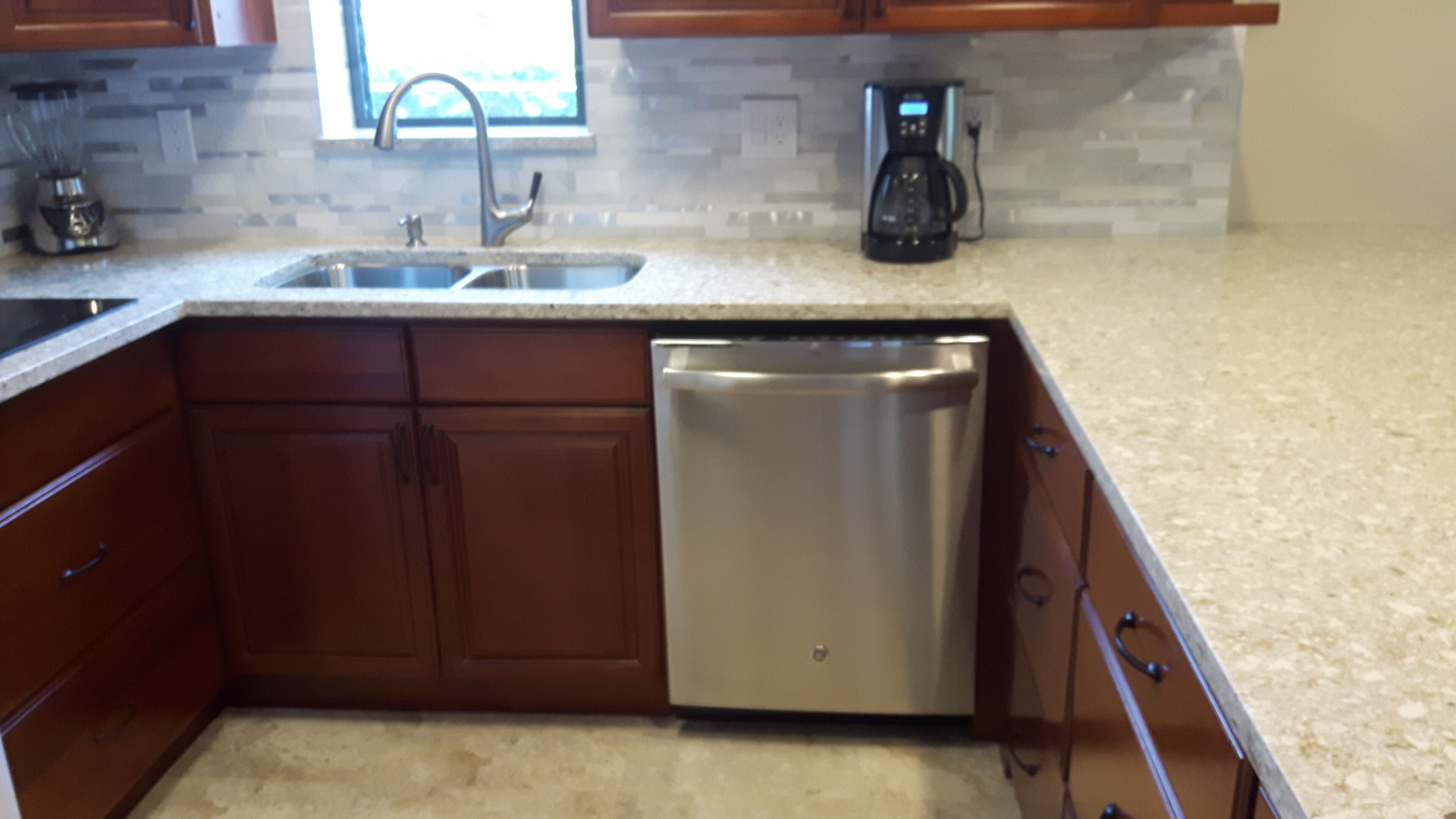 A kitchen with wooden cabinets, a stainless steel dishwasher, a sink, and a coffee maker.