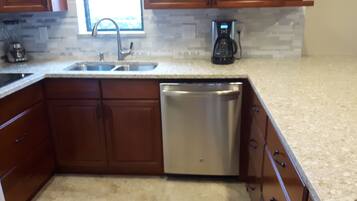 A kitchen with wooden cabinets, a stainless steel dishwasher, a sink, and a coffee maker.