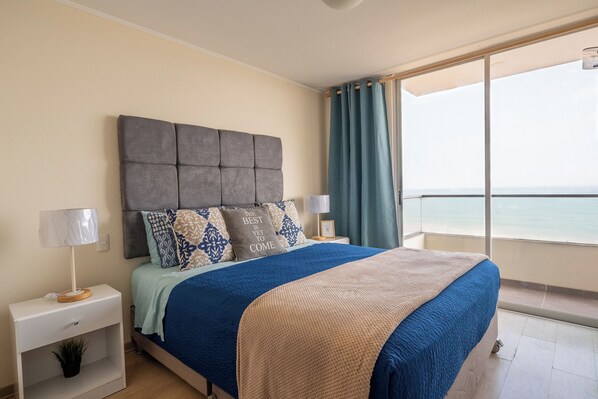 A bedroom with a large bed, a nightstand, a lamp, and a view of the sea through a window. - Need Vitamin Sea??? 2br/2baths (San Miguel)
