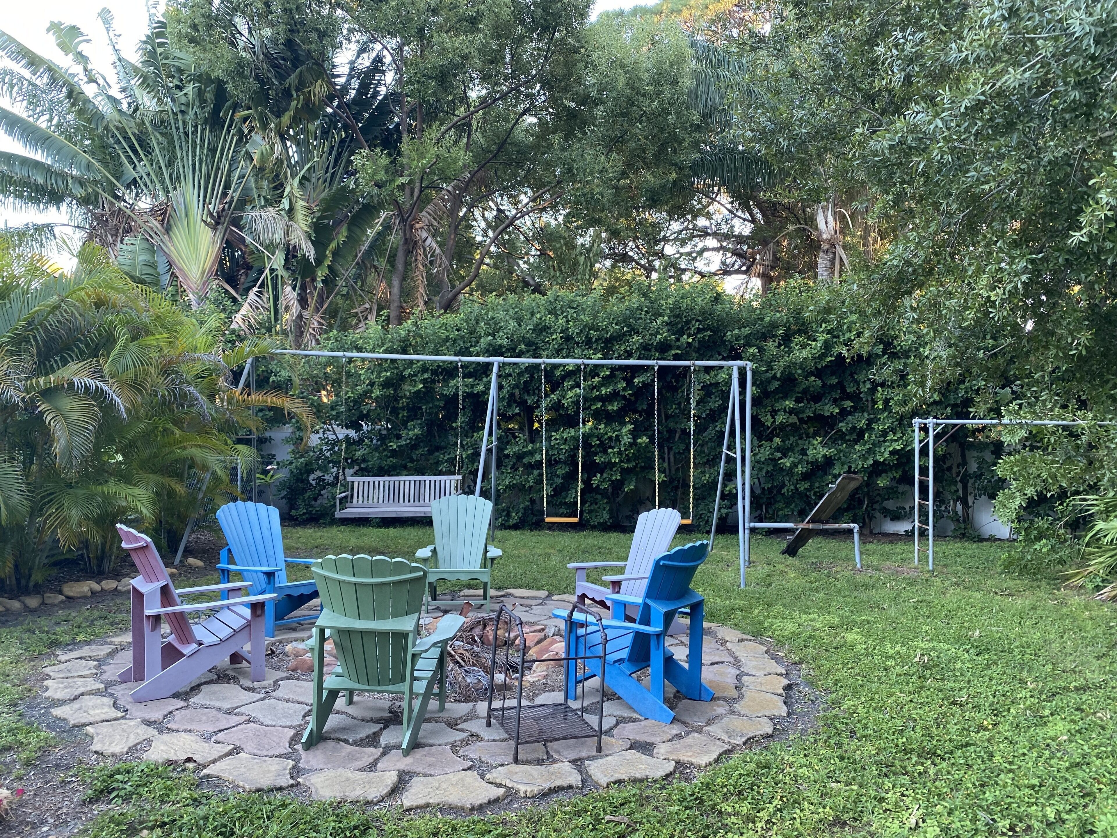 A patio with Adirondack chairs, a swing set, and a fire pit.