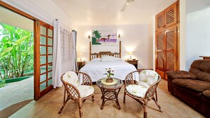 Un dormitorio con cama, ventilador de techo, mesita de noche, una mesa con sillas y vistas a zonas verdes a través de una puerta corrediza.