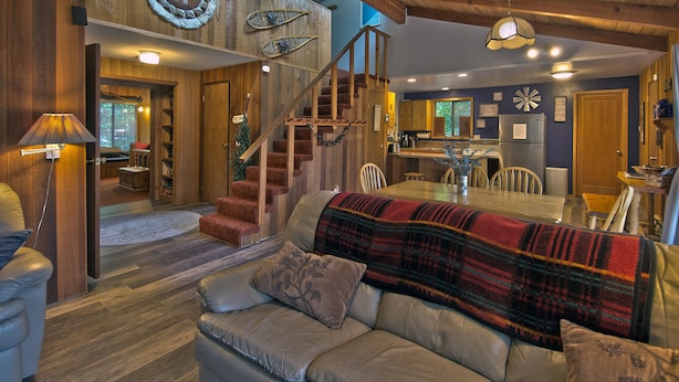 A cozy interior with a wooden staircase, a dining area, and a living room with a sofa and a blanket. - The Lyons Den at Upper Timberline Village (Packwood)