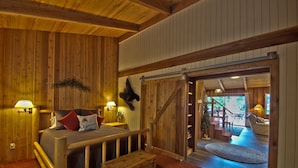 A wooden interior with a bed, two lamps, a mounted animal head, and a view to a balcony. - The Lyons Den at Upper Timberline Village (Packwood)