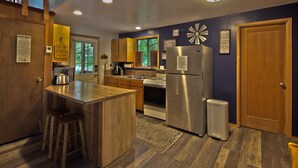 A modern kitchen with wooden cabinets, stainless steel appliances, and a bar area. - The Lyons Den at Upper Timberline Village (Packwood)