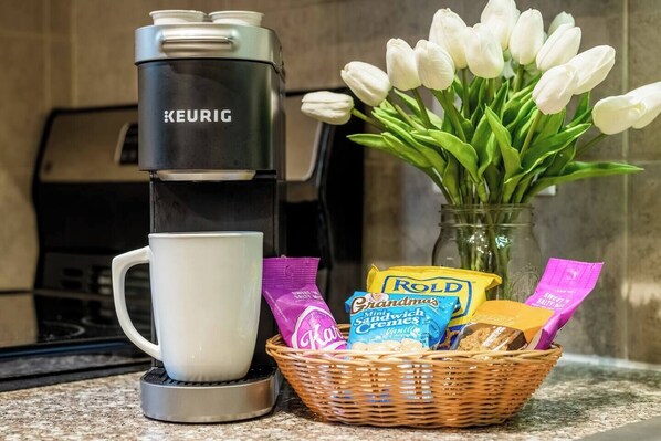 A Keurig coffee maker, a white mug, a basket with snacks, and a vase with white tulips. - PEACEFUL SPA ESCAPE MINUTES TO MOHEGAN SUN CASINO (Norwich)