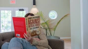 Una persona sentada en un sofá leyendo un libro titulado 'Against Medical Advice' de James Patterson y Hal Friedman.