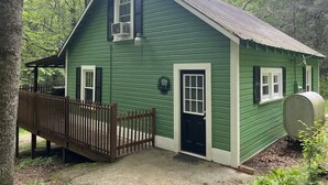 Een groene houten chalet met een veranda, een zwarte deur en een klein raam.