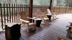 Una terraza de madera con sillas Adirondack y un banco, rodeada por una valla de madera.