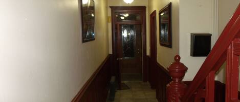 A narrow hallway with wooden wainscoting, a tiled floor, and a staircase with a red handrail.