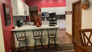 Cocina moderna con armarios blancos, una isla de mármol con taburetes y una pared de acento roja.