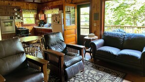 Interior acolhedor de uma cabana com área de jantar, cozinha e sala de estar com uma grande janela.