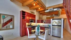 Una cocina moderna con gabinetes rojos, electrodomésticos de acero inoxidable y una mesa de comedor de vidrio.