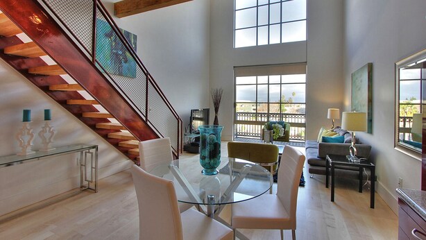 Una sala de estar moderna con una mesa de vidrio, sillas blancas, un sofá y una escalera con barandas de madera.