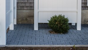 A white metal gate with a small bush in front, a brick wall behind, and a blue sign on the wall.