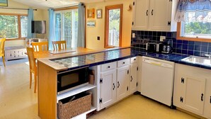 A kitchen with white cabinets, a blue tiled countertop, a ceiling fan, and a dining area with a table and chairs.