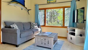 A living room with a sofa, a coffee table, a mounted fish, a TV, and a window with curtains.