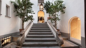 Eine Steintreppe mit aufwendiger Balustrade, gesäumt von Topfpflanzen, die zu einem Innenraum mit warmem Licht führt.