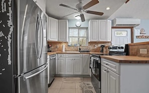 A kitchen with white cabinets, a stainless steel refrigerator, a ceiling fan, and a window.