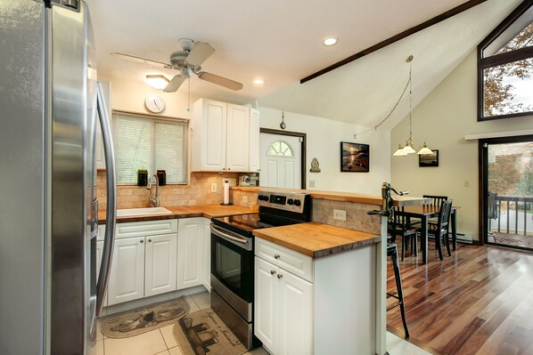 Una cocina con armarios blancos, un refrigerador de acero inoxidable, una encimera de madera y una zona de comedor con mesa y sillas.