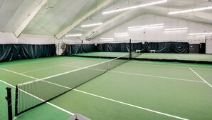 Una cancha de tenis interior con red, suelo verde y líneas blancas.