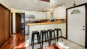 Una cocina con piso de madera, gabinetes blancos, un refrigerador de acero inoxidable, un microondas y una isla de madera con taburetes de bar.