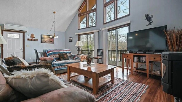 Un salón espacioso con techo alto, ventanas amplias, una mesa de centro de madera, un sofá y un televisor.