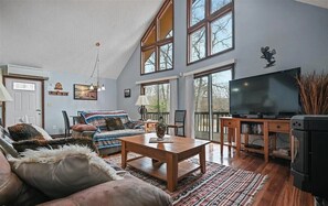 Un salón espacioso con techo alto, ventanas amplias, una mesa de centro de madera, un sofá y un televisor.