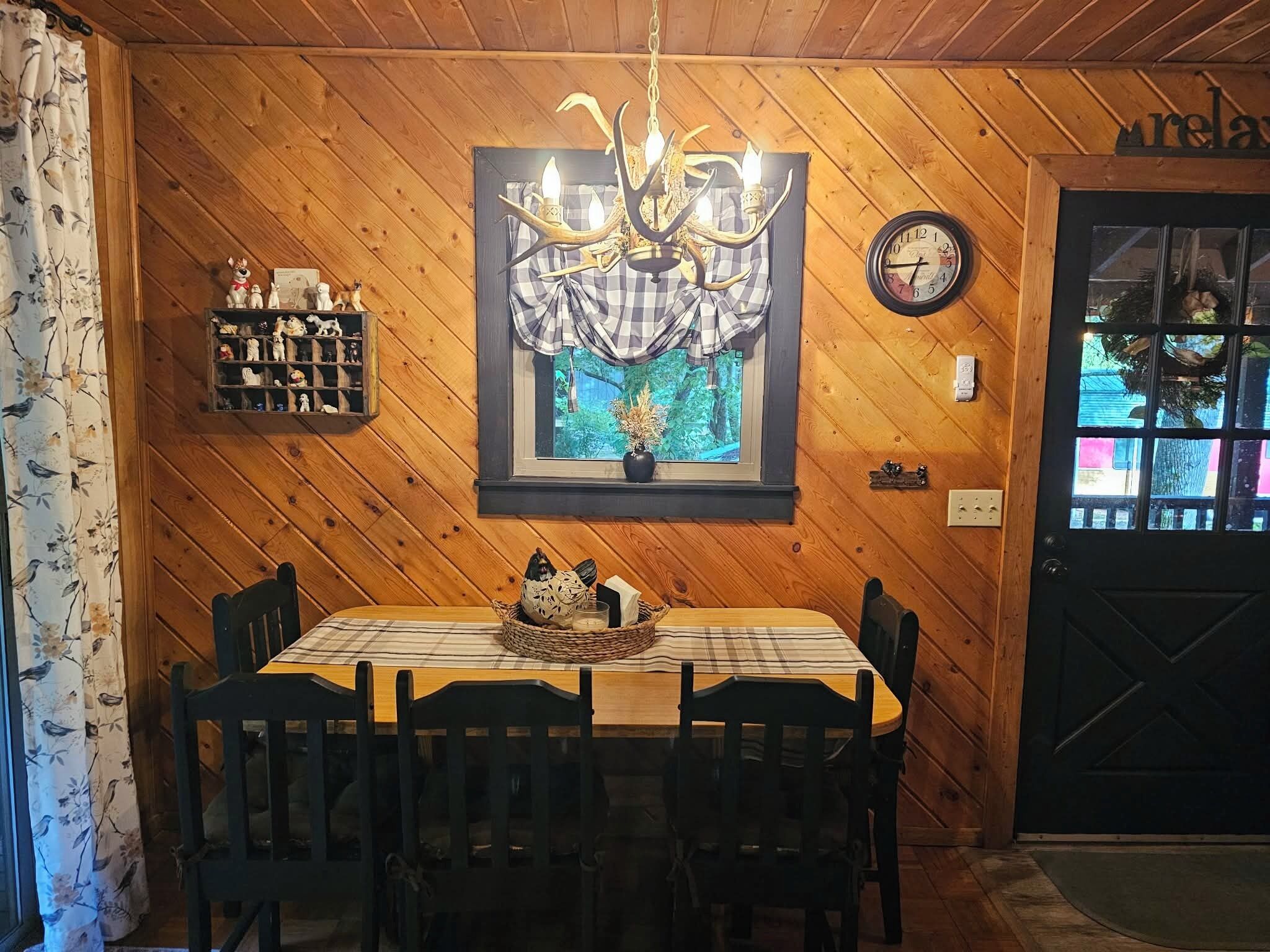 Puisilla paneeleilla verhoiltu huone, jossa on pöytä, tuoleja, kattokruunu, kello ja ikkuna, josta on näkymä.
