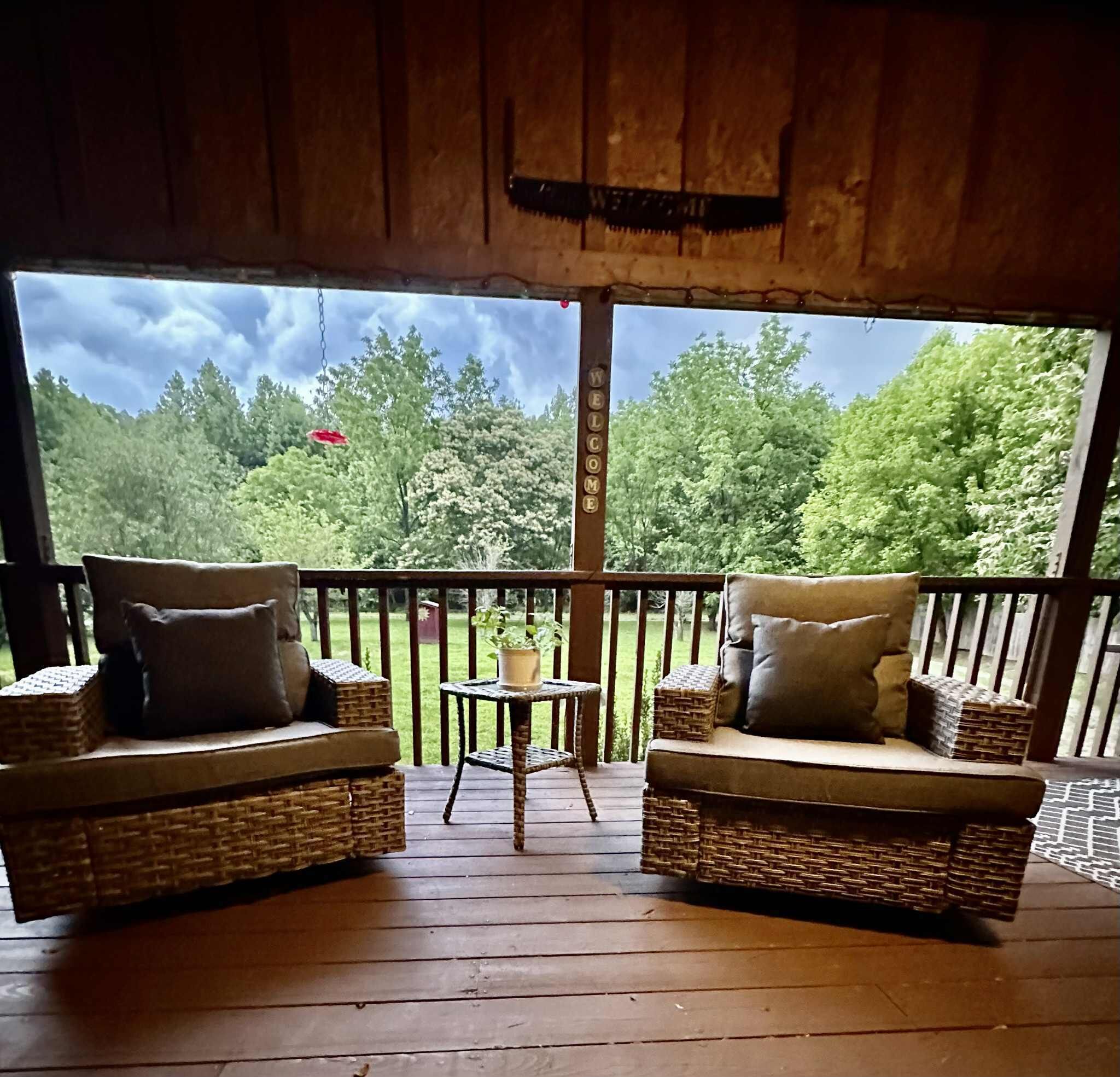 Une terrasse en bois, agrémentée de meubles en osier et d’une petite table, donnant sur une zone boisée.