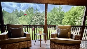 A wooden deck with wicker furniture and a small table, overlooking a forested area. - Relax at Clear Creek Family Retreat – Cozy Ellijay Cabin by the Water (Ellijay)
