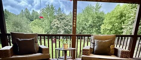 Une terrasse en bois, agrémentée de meubles en osier et d’une petite table, donnant sur une zone boisée.