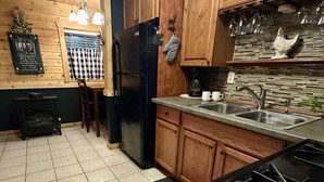 A kitchen with wooden cabinets, a black refrigerator, a stove, and a tiled floor. - Relax at Clear Creek Family Retreat – Cozy Ellijay Cabin by the Water (Ellijay)