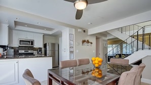 A modern kitchen with white cabinetry, a dining area with a glass-top table, and a staircase with a glass railing. - Dana Point Vacation Rental Close To The Beach! (Dana Point)