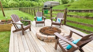 A wooden deck with Adirondack chairs and a stone fire pit.