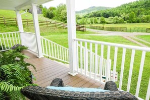 A porch with a view of a green landscape, white railings, and a wicker chair.