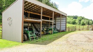 A barn with a covered open area, green tractors inside, and a fenced pasture area.