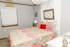 Een slaapkamer met een bed, nachtkastje, lamp, lijst met afbeelding en raam met zonwering.