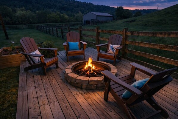 A wooden deck with a fire pit and four Adirondack chairs.