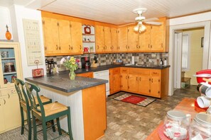 Een keuken met houten kastjes, een centraal eiland met stoelen, een plafondventilator en een rood vloerkleed.