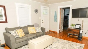 A living room with a grey sofa, a cream-colored ottoman, and a patterned rug.