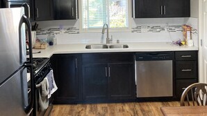 A modern kitchen with dark cabinetry, a stainless steel refrigerator, a dishwasher, and a wooden dining table. - Dog Friendly, Allergen-free 5 minute walk to the bay and eateries (Los Osos -Baywood Park)